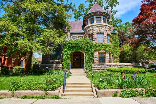 Historic stone house with ivy in Fort Wayne, nestled in a lush garden under clear skies.