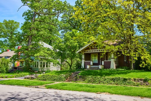 Sunlit suburban charm in Fort Wayne, featuring two distinct, historic homes amidst lush greenery.
