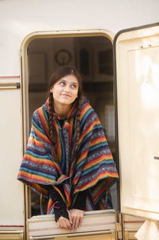 A beautiful girl in a hippie ensemble poses against the backdrop of a trailer in the park. High quality photo