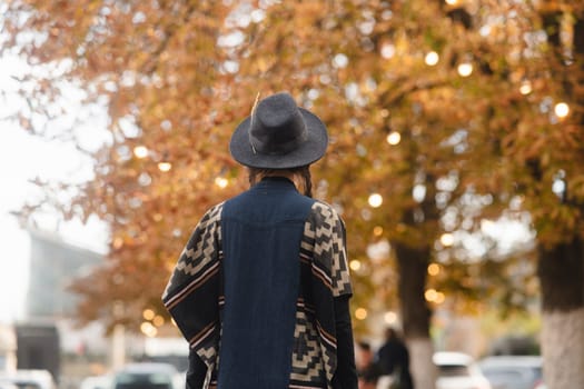 A lovely lady exudes boho chic, adorned with a black hat, amidst the autumnal cityscape. High quality photo