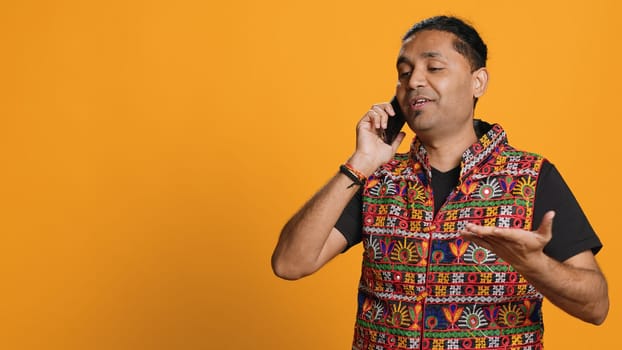Man discussing with best friend over telephone call, enjoying leisure time. Upbeat person wearing indian attire talking with mate in phone call, isolated over studio backdrop, camera A