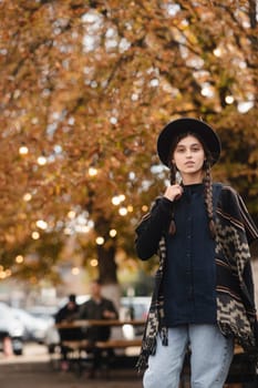 A fashionable girl showcases boho elegance, topped with a black hat, amidst the autumn city streets. High quality photo