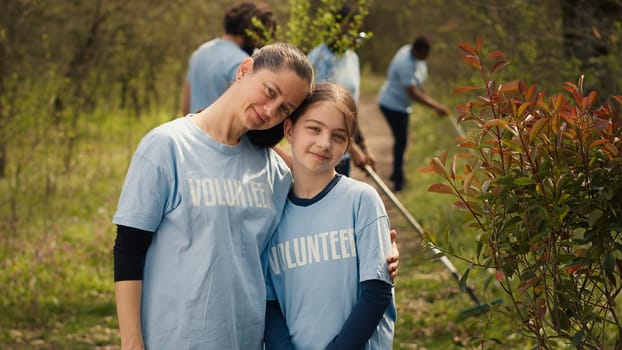 Portrait of mother and daughter volunteering to clean up a forest area, showing a sense of devotion and responsibility for the natural environment conservation. Ecological justice. Camera A.
