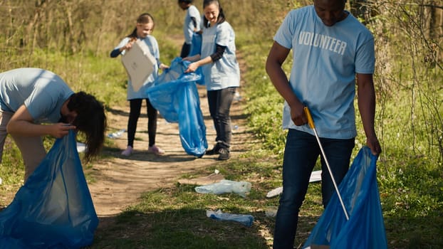 Eco friendly activist grabbing garbage and plastic waste from a forest area, cleaning up the woods and collecting rubbish in a trash bag. Man volunteer dealing with waste management. Camera A.