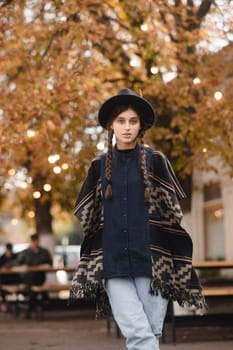 A charming woman, embracing boho fashion, completes her ensemble with a black hat in the autumn city. High quality photo