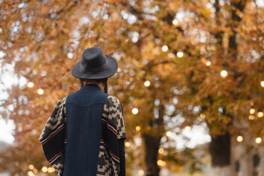 A stunning young woman, channeling bohemian vibes, dons a black hat in the autumn city streets. High quality photo