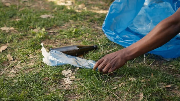 People supporting cleanup of the natural environment by grabbing recyclables and trash objects from the woods, collecting in a garbage bag. Using utensils to pick up rubbish. Close up. Camera A.