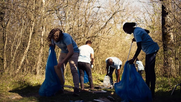 Team of volunteers collecting rubbish to fix pollution problem within the habitat, protect the natural environment. Activists doing voluntary work to clean the woods from trash. Camera B.