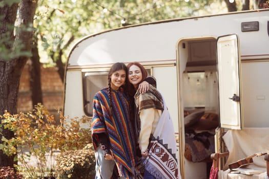 Two chic ladies embrace hippie fashion with a trailer as their backdrop. High quality photo