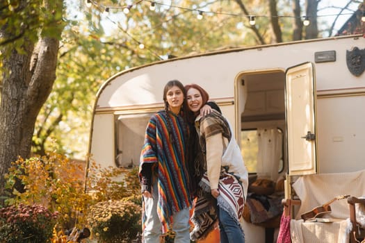Two stylish girls in hippie attire pose against the backdrop of a trailer. High quality photo