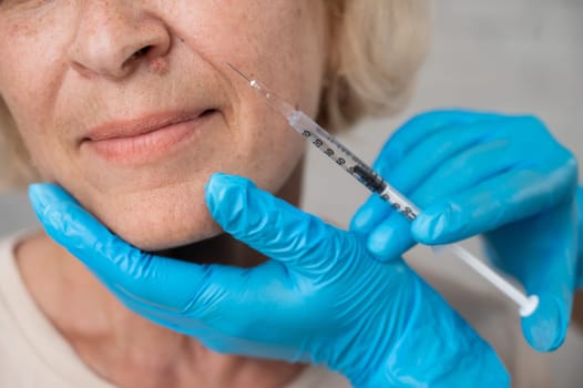 Doctor makes beauty injections in the face of an old caucasian woman. Cropped portrait