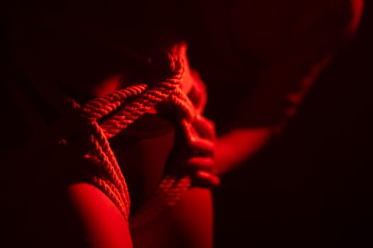 Man tightens ropes using Japanese shibari technique on woman's body in red light