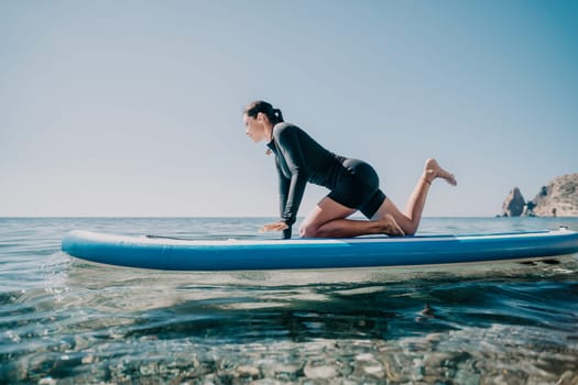 Woman sup yoga. Middle age sporty woman practising yoga pilates on paddle sup surfboard. Female stretching doing workout on sea water. Modern individual hipster outdoor summer sport activity