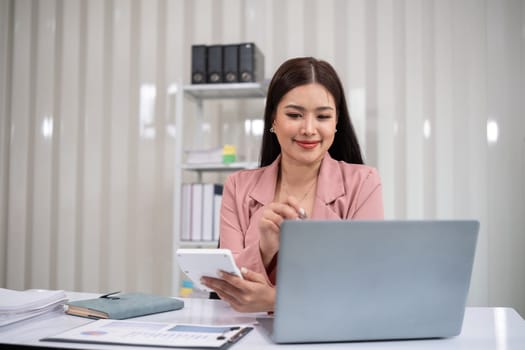 Asian businesswoman working on financial document with laptop on desk in office room.