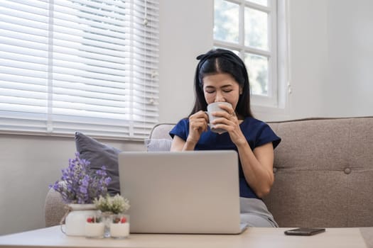 Happy Asian retired woman in her 60's enjoying social media on laptop while relaxing in living room..