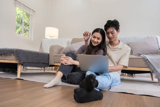 Young Asian couple in love Sitting happily together looking at laptop and relaxing in the living room. Couple making romantic love in the living room.