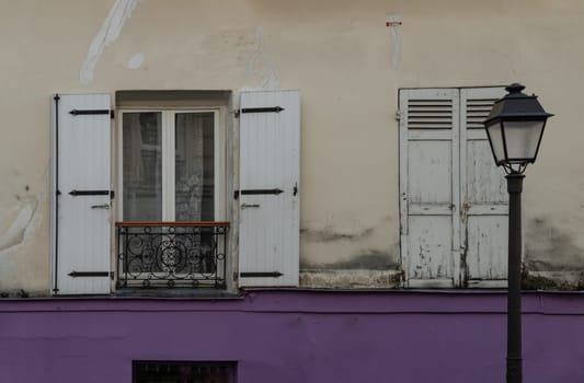 France, Paris - Jan 03, 2024 - Shutters and open window with lace curtained on old wall of a ground floor residence and street lantern. Space for text, Selective focus.