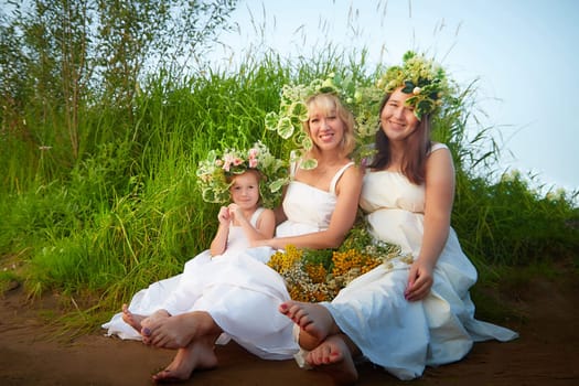 Ivan Kupala Celebration. Portrait of Girls With Floral Wreaths by the River at Sunset. Family clad in white dresses celebrate at dusk