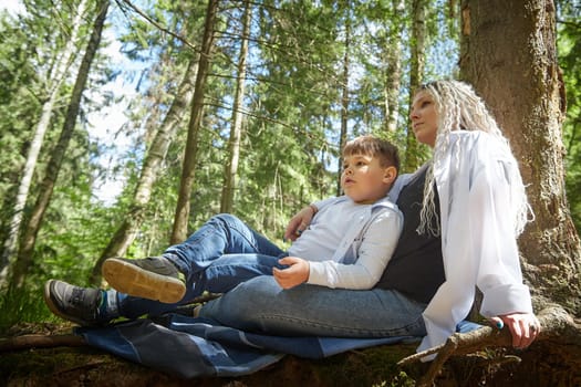 Funny mother with dreadlocks and fat boy happy resting in forest on a sunny summer day