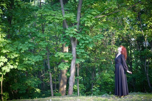 Elegant senior mature Woman dancing in Black Dress in green park. Woman with red hair posing on nature