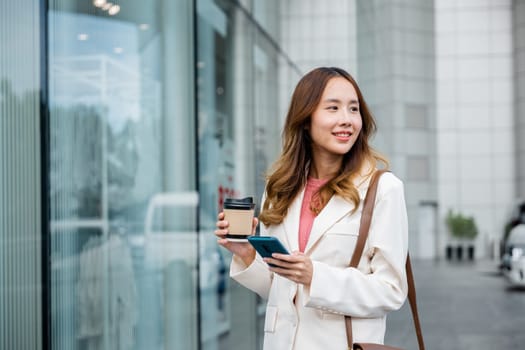 Busy businesswoman juggling coffee and cell phone, staying connected while walking to work in the morning.