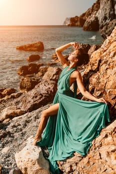 Woman green dress sea. Woman in a long mint dress posing on a beach with rocks on sunny day. Girl on the nature on blue sky background