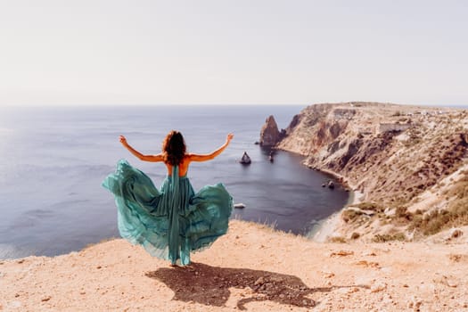 Woman green dress sea. Female dancer posing on a rocky outcrop high above the sea. Girl on the nature on blue sky background. Fashion photo