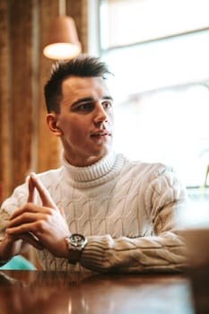 A man is sitting at a table, with both of his hands raised up in the air. His body language appears expressive and engaged, as if he is responding to something exciting or surprising.