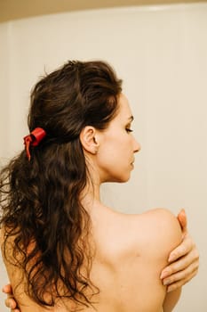 A woman with long hair is wearing a red ribbon in her hair. She is looking at something in the mirror