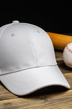 Baseball cap, ball and bat on wooden background close up