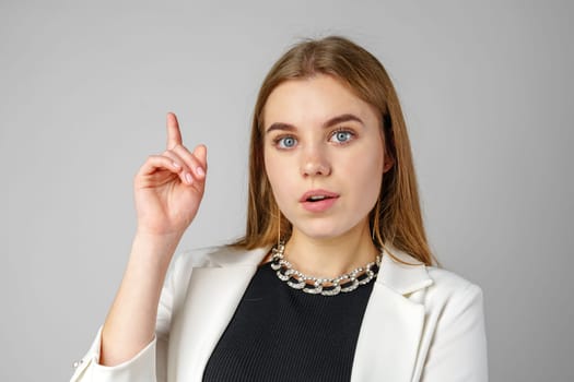 Thoughtful Young Woman in a Stylish White Blazer Posing on gray background close up