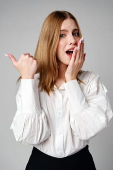 Young blonde woman in formal outfit pointing to the side against gray background in studio