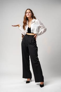 A woman stands wearing a white shirt and black pants. She is posing for the camera in a casual outfit, exuding confidence and style.