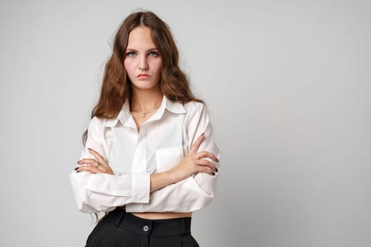 woman is standing wearing a white shirt and black pants. She has a confident stance and is looking directly at the camera.