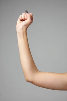 A single human arm is raised in a clenched fist, symbolizing determination, strength, and unity. The arm is displayed against a neutral gray backdrop, highlighting the muscular form and skin texture. The focused composition emphasizes the power of human expression through gesture.