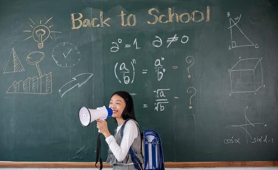 A girl is standing in front of a chalkboard with the words Back to School written on it. She is holding a megaphone and smiling