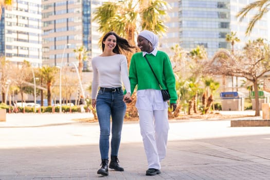young multiracial couple of two women walking smiling happy through the city holding hands, concept of diversity and modern lifestyle