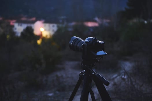 A digital camera with black mockup touch screen placed on tripod by a travel photographer hiker, capturing the beautiful view of a city in mountains at sunrise. The concept of World photography Day