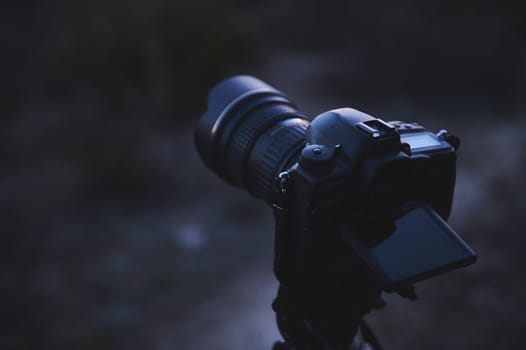 World Photography Day concept. A modern digital semi-mirror camera with a movable touch screen, mounted on a tripod in the nature, ready to take steady shots, pictures, photos or videos. Close-up