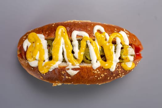 Hot dog sausage in a bun with sauces, isolated on a gray background.