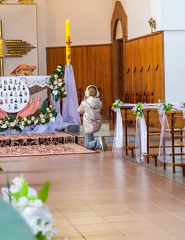 Shot of girl, wearing headphones, kneeling at the altar at Roman catholic church, says prayer and taking pictures of the altar