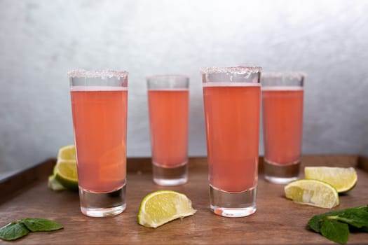 four pink cocktails with limes on a wooden stand.