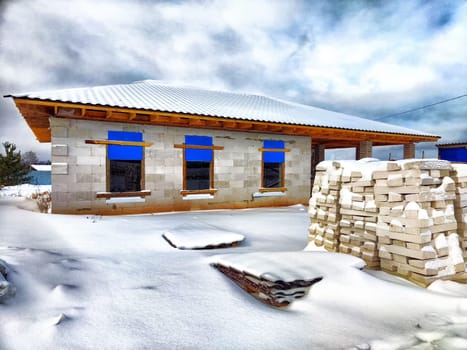 An unfinished house and building materials in the snow. Building a new house in winter. An unfinished house with building materials surrounded by snow