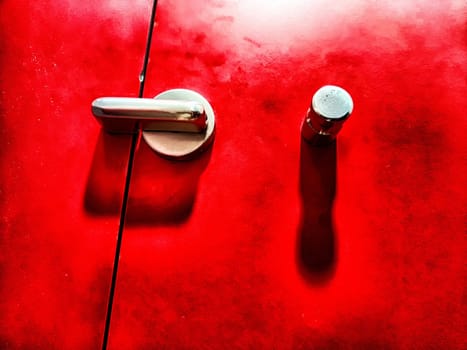 Close-up of a shiny metallic door handle and a latch set against a crimson backdrop. Close-Up of Chrome Handle and Latch on a Vibrant Red Door