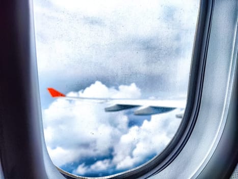 Clouds and a wing through a porthole in an airplane. Aerial View of Fluffy Clouds and Airplane Wing From Cabin Window. Wing above vibrant cloud. Blurred
