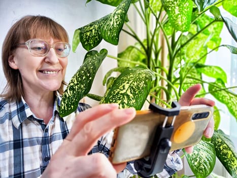 Smiling woman in glasses using a smartphone on a tripod for a video chat. A middle-aged woman posing and taking a selfie