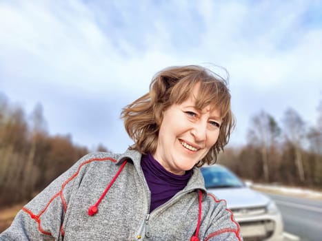 A woman takes a selfie on the road near a car. The concept of car travel. A woman captures a selfie with her car in the background during road trip