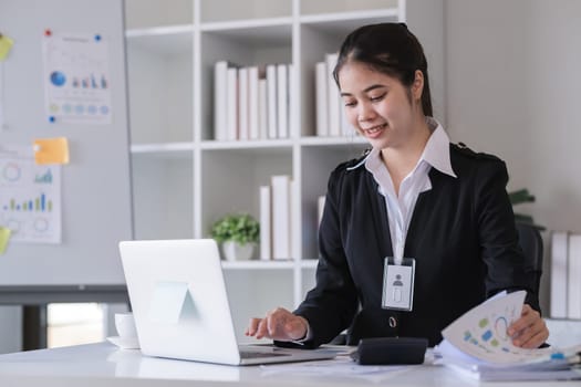 Accountant sitting with financial documents, using laptop, calculating financial and tax figures for company on table in office.