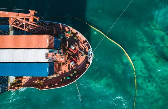 Aerial view of a container cargo ship stands aground after a storm with floating boom around the ship to prevent the spread of petroleum. Top down view of a ship bow