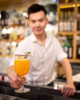 Bartender on the bar stretches out an orange cocktail.